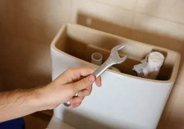 Mano con una llave sobre el mecanismo de una cisterna